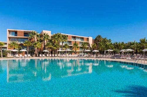 a large blue swimming pool with chairs and umbrellas at Apartamentos Herdade dos Salgados in Albufeira