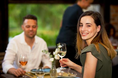 a woman sitting at a table holding a glass of wine at Hotel Vineyard Inn - Szőlőskert in Nagykanizsa
