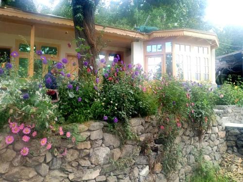 a stone retaining wall with flowers in front of a house at Mountain Refuge Guest House in Baltit