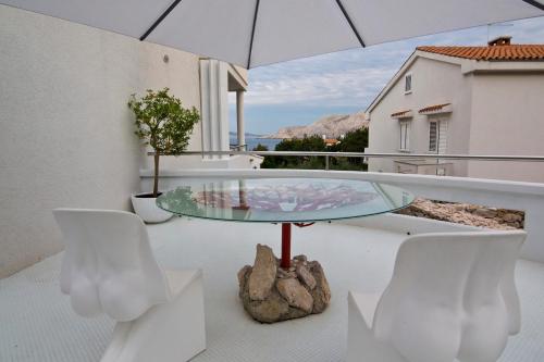 een glazen tafel en stoelen op een balkon met een parasol bij Villa Perla Baska in Baška