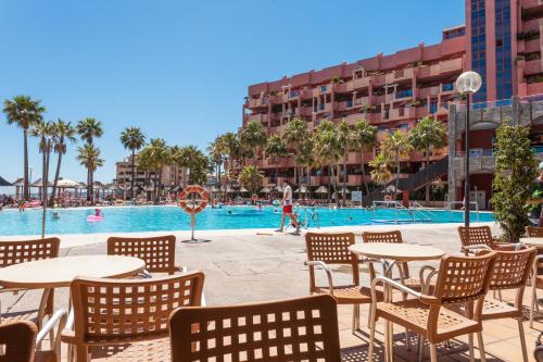 a pool with tables and chairs in front of a hotel at Holiday World Polynesia in Benalmádena