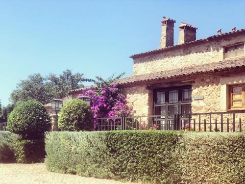 an old stone house with a hedge in front of it at Apartamentos Rurales La Macera **** in Valencia de Alcántara