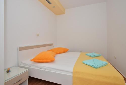 ein weißes Bett mit orangefarbenen und blauen Kissen darauf in der Unterkunft Apartments Jovic in Makarska