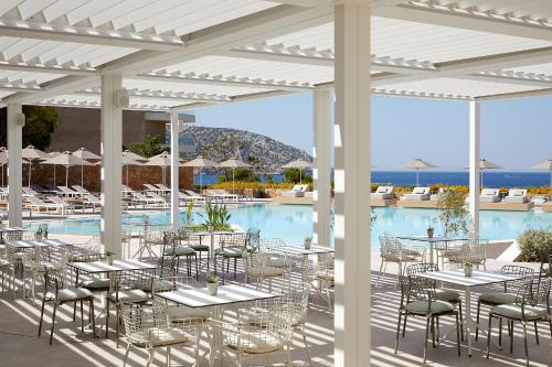 eine Terrasse mit Tischen und Stühlen neben einem Pool in der Unterkunft Vincci EverEden in Anavyssos