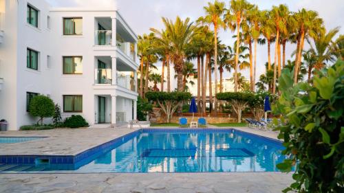 a swimming pool in front of a building with palm trees at Rododafni Beach Apartments in Paphos City