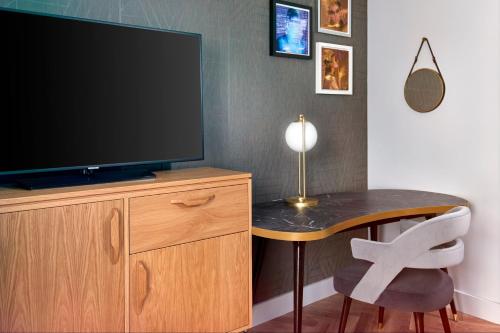 a television on a wooden cabinet with a table and a chair at NYX Hotel London Holborn by Leonardo Hotels in London
