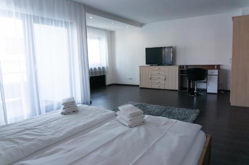 a white bedroom with a bed and a tv at Eisberg Gästehaus & De Luxe Appartements in Friesenheim
