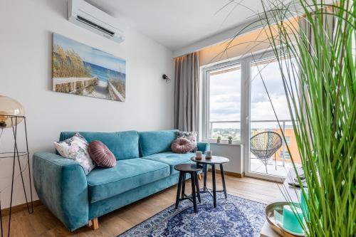 a living room with a blue couch and a large window at Symphony Baltica Towers Aparthotel in Gdańsk