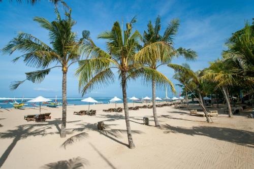 a beach with palm trees and chairs and umbrellas at Tandjung Sari Hotel in Sanur
