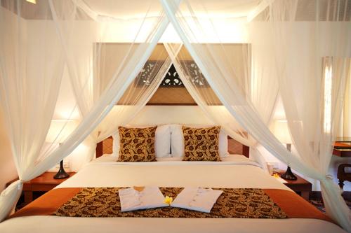 a bedroom with a bed with white curtains at Tandjung Sari Hotel in Sanur