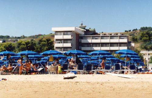 a group of people sitting on a beach with blue umbrellas at Hotel Palmarosa in Roseto degli Abruzzi