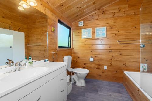 a bathroom with wooden walls and a toilet and a sink at Pearl Retreat - Mangawhai Heads Holiday Home in Mangawhai