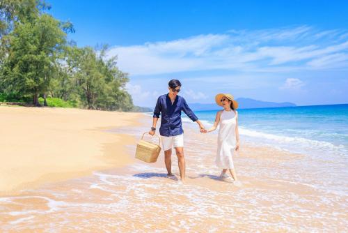 a man and woman holding hands while walking on the beach at JW Marriott Phuket Resort and Spa in Mai Khao Beach