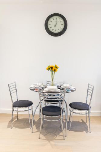 a dining room table with chairs and a clock on the wall at Cosy 1 Bed Apartment in Centre of St Albans - FREE Parking - 5 min walk to St Albans city centre & Railway station - Big Savings on Longer Stays!! in St. Albans