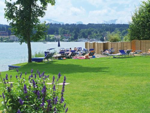 a group of people laying in chairs on the grass by the water at Barry Memle Directly at the Lake in Velden am Wörthersee