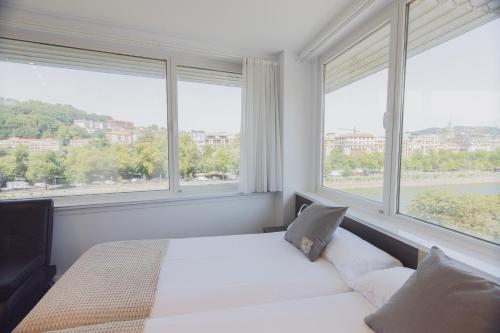 a bedroom with a bed and two large windows at Pensión Riberas del Urumea in Donostia-San Sebastián