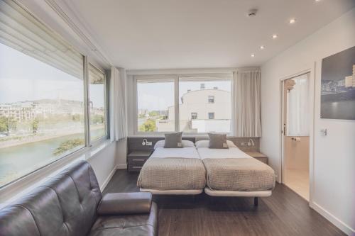 a bedroom with a bed and a couch and windows at Pensión Riberas del Urumea in San Sebastián