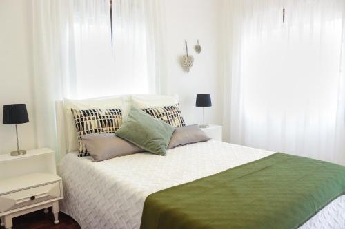 a bedroom with a bed with a green blanket and two windows at Ascensor House in Nazaré