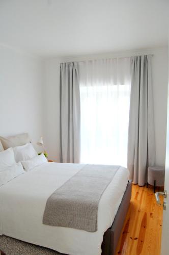 a bedroom with a large white bed with a window at Verde'Água Family Home in Mosteiros