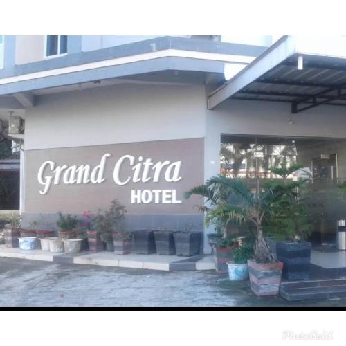 Hotel Grand Citra Prabumulih في Perabumulih: علامة على فندق كبير شيارة مع نباتات الفخار