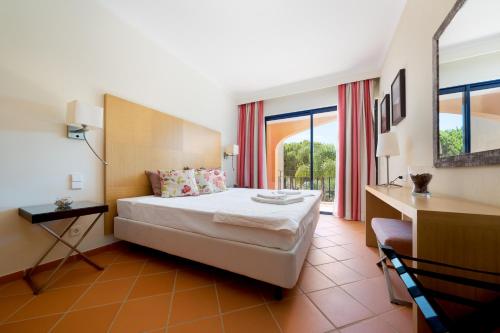 a hotel room with a bed and a desk and windows at AL - Apartamentos Vila Sol F5 Bloco 3 in Quarteira