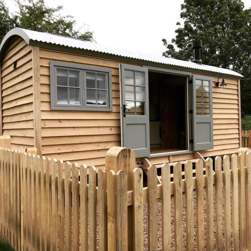 une petite maison derrière une clôture en bois dans l'établissement Astwell Mill Luxury Shepherds Hut, à Helmdon