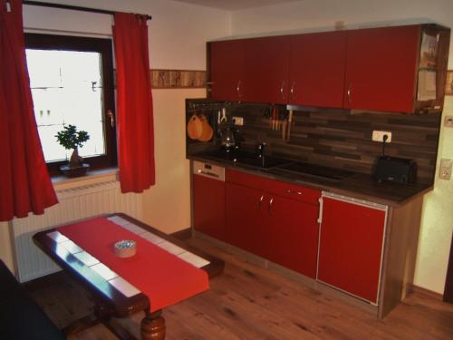 eine Küche mit roten Schränken, einem Tisch und einem Fenster in der Unterkunft Doppelzimmer Liliensteinblick 1.OG in Bad Schandau