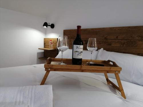 Una botella de vino y dos vasos en una bandeja en una cama. en Hostal Cuéntame Evolución Auto Check in en Burgos