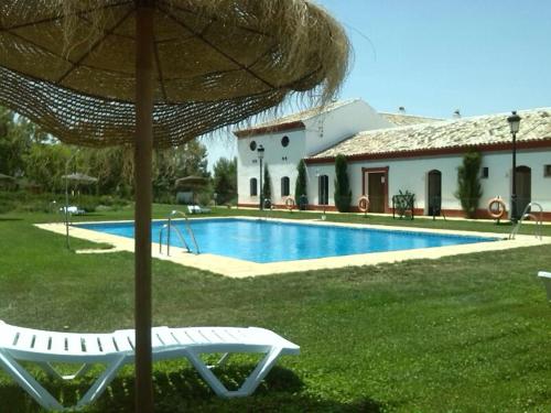 a pool with a chair and an umbrella next to a house at Complejo Pueblo Blanco in Olvera