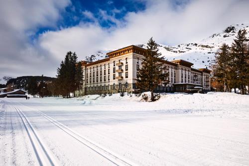 a large building in the snow in front of a mountain at Maloja Palace Suites CO2-Neutral in Maloja