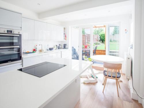 a white kitchen with a counter and a table at Modern & Peaceful Family Home with Private Garden in London