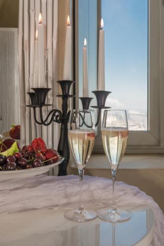 two glasses of wine on a table with a plate of fruit at Mythical Blue Luxury Suites in Fira