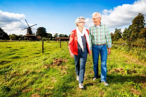 an older couple walking in a field with a windmill at Stadshotel Rijssen in Rijssen