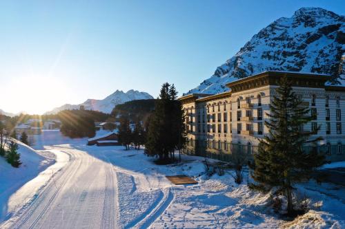 a building in the snow with a mountain in the background at Maloja Palace Suites CO2-Neutral in Maloja