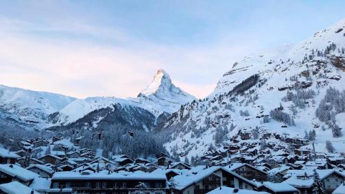 een berg bedekt met sneeuw met een stad en gebouwen bij Hotel Capricorn in Zermatt