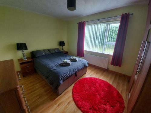 a bedroom with a bed with a red rug and a window at HOMELY YELLOW BUNGALOW -Articlave-near Castlerock in Castlerock