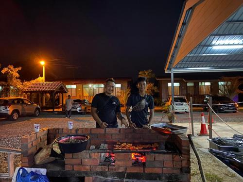 two men standing in front of a brick grill at Tamteh Homestay in Ayer Hitam