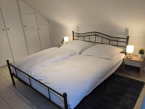 een groot bed met witte lakens en 2 lampen op tafels bij Ferienwohnung Zundel in Neu-Anspach