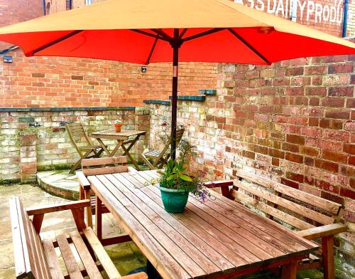 a wooden table with a red umbrella and a potted plant at Cotswold Place in Cirencester