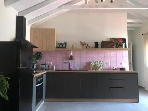 a kitchen with black cabinets and a pink tile wall at Rigo’s apartment in Platamonas