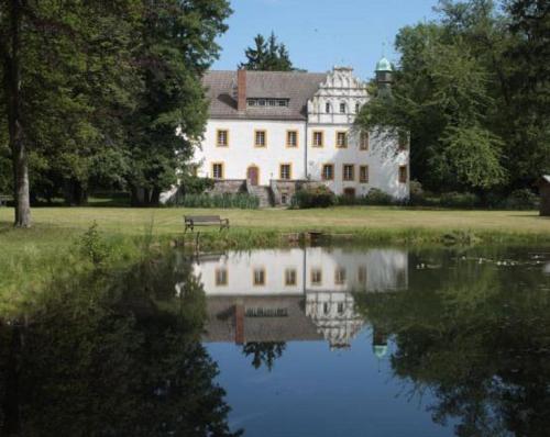 ein großes weißes Haus mit Reflexion im Wasser in der Unterkunft Schlossparkhotel Sallgast in Sallgast