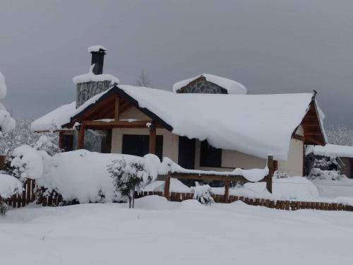 a house covered in snow with a fence at Cabañas Boca del Chimehuín in Junín de los Andes