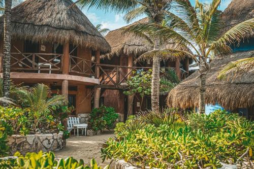 a resort with a building with thatched roofs and palm trees at La Conchita Tulum in Tulum
