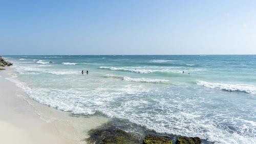 a beach with people in the water and waves at La Conchita Tulum in Tulum