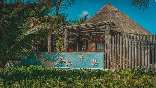 a house with a thatched roof and a fence at La Conchita Tulum in Tulum