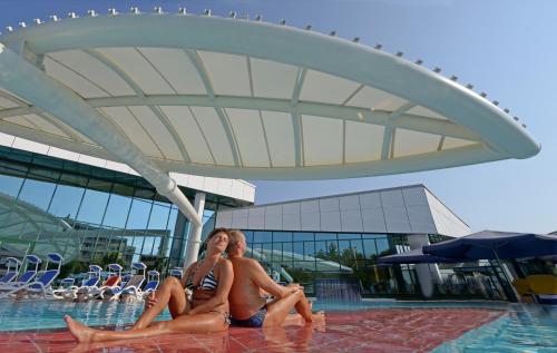two people sitting next to a swimming pool at Hotel Reindl Suiten & Appartments in Bad Füssing