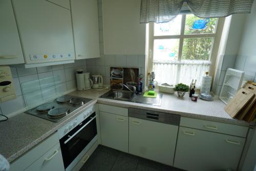 a kitchen with white cabinets and a sink and a window at Günnis Perle am Harleufer in Carolinensiel