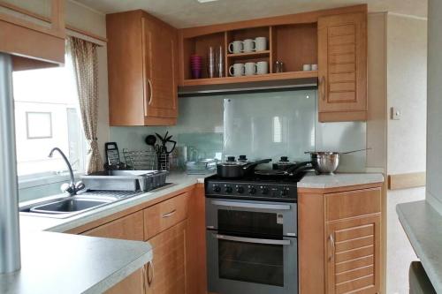 a kitchen with wooden cabinets and a stove top oven at Beachside, Family-friendly, WiFi, 8 berth Caravan 133 in Skegness