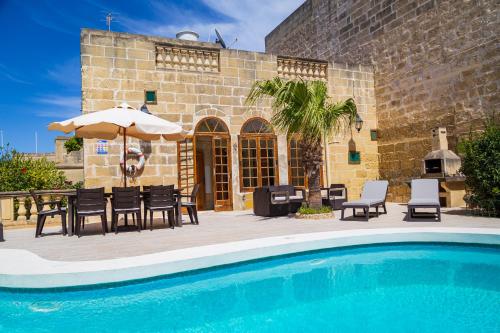 una piscina con sillas y una sombrilla junto a un edificio en Dar ta' Tumas, en Għarb