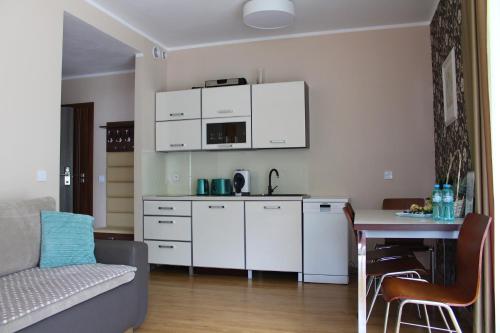 eine Küche mit weißen Schränken, einem Tisch und einer Couch in der Unterkunft Apartament Mariva B03 z ogródkiem - Pobierowo - blisko morza - przy kompleksie Grand Laola SPA in Pobierowo